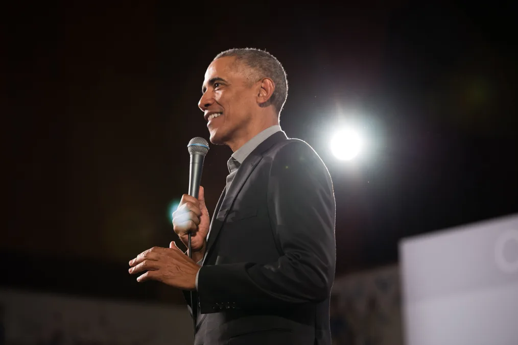 President Obama smiles while holding a microphone, looking left.