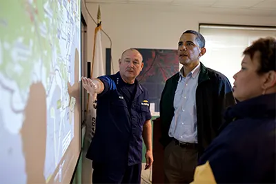 President Obama looks at a projected map with two people with light-medium skin tones.