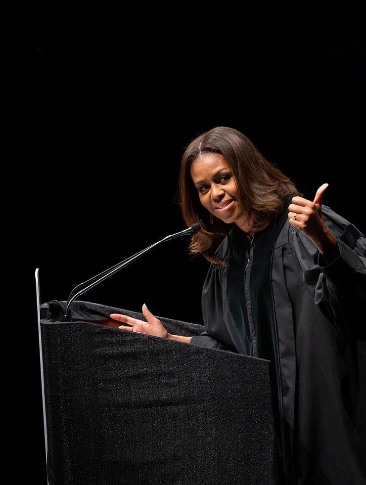 Michelle Obama speaks on a stage with a black gown on