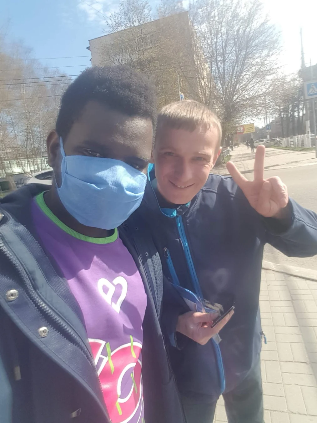 Two young men take a selfie, one throwing up a peace sign.