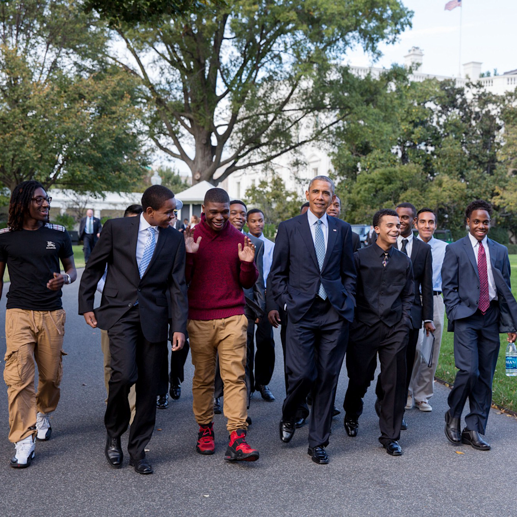 On the South Lawn, President Obama walks in the middle of a group of young men who are members of the Obama Foundation’s My Brother’s Keeper program. All have a range of light to deep skin tones. They are wearing a mix of casual and professional attire. 