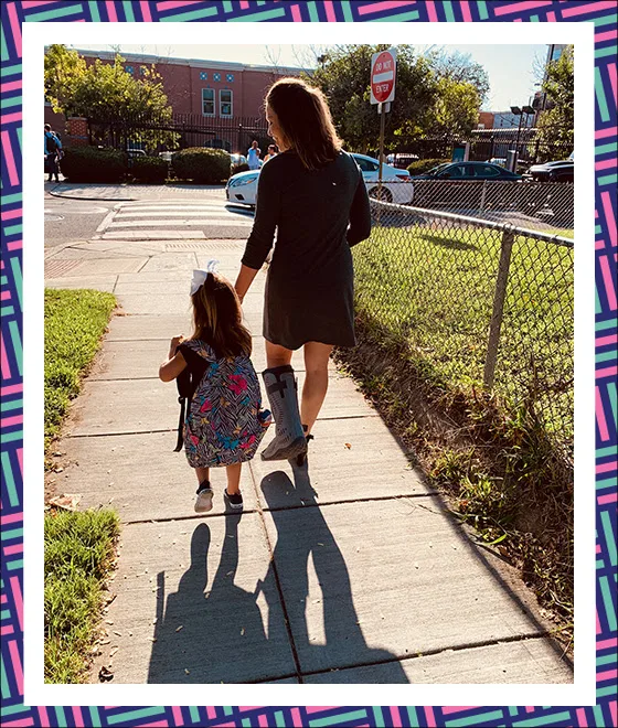 A woman with a light skin tone walks her young daughter to school. 