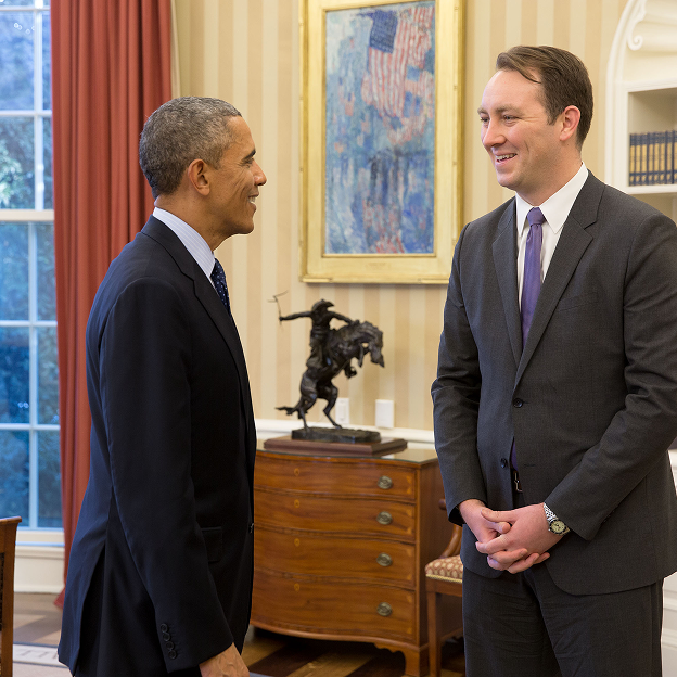 President Obama stands in the Oval Office alongside Robert Diamond, a man with a light skin tone and brown hair. Both men are wearing suits. 