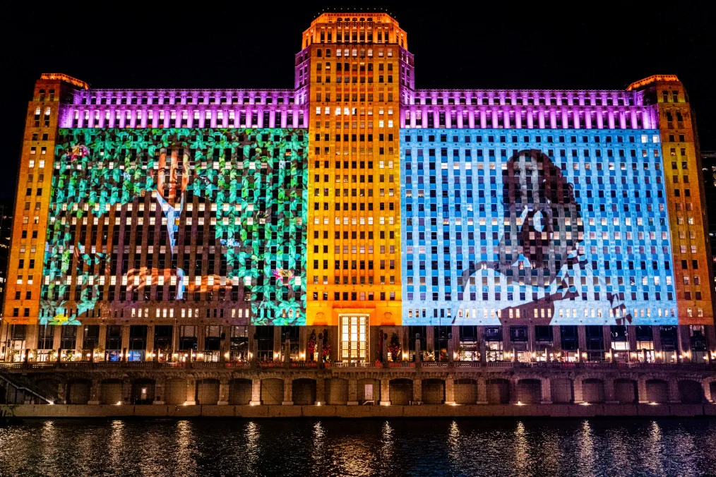 A building with various colors of orange, blue, green, and pink showing Barack Obama and Michelle Obama on either side of the building infront of water 