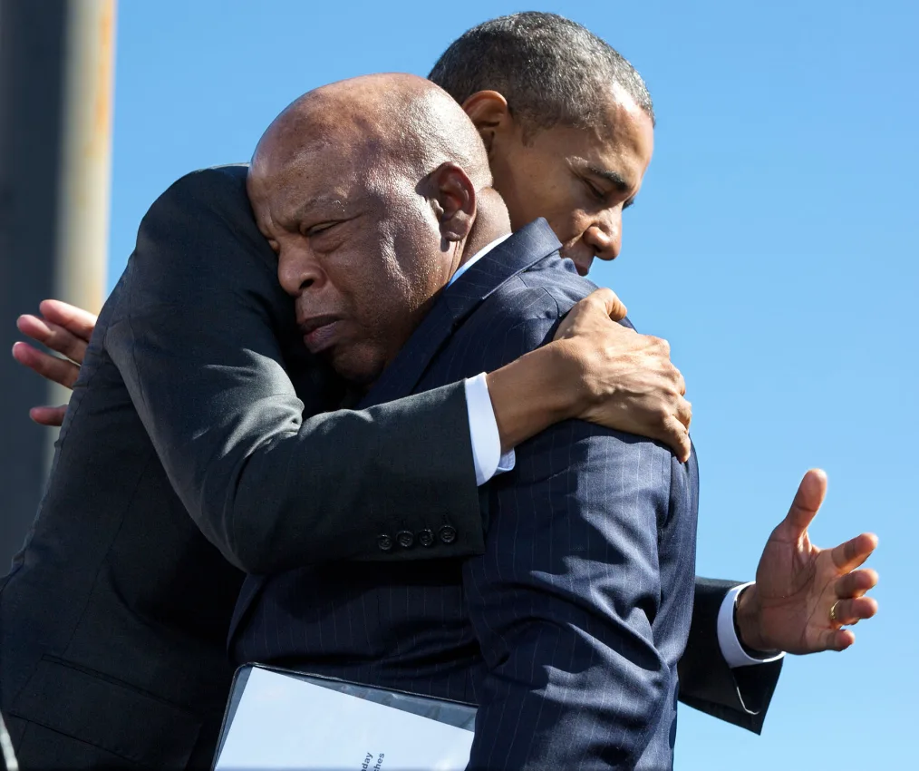Barack Obama a black man wearing a black suit hugging another black man with medium brown skin wearing a blue stripe suit