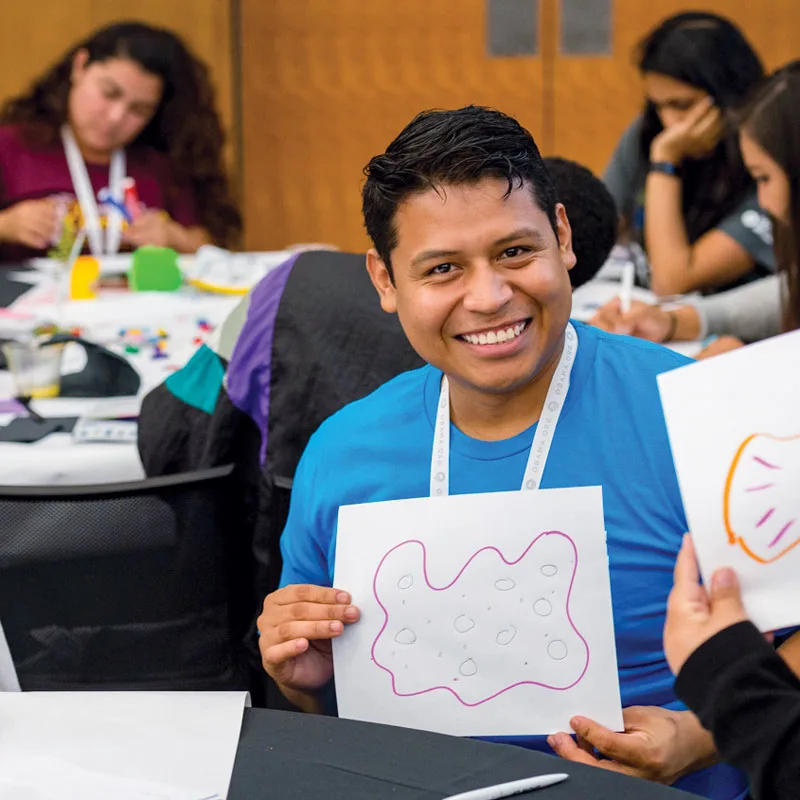 A young man holds up a drawing and smiles during an Obama Foundation Training Day in 2017.