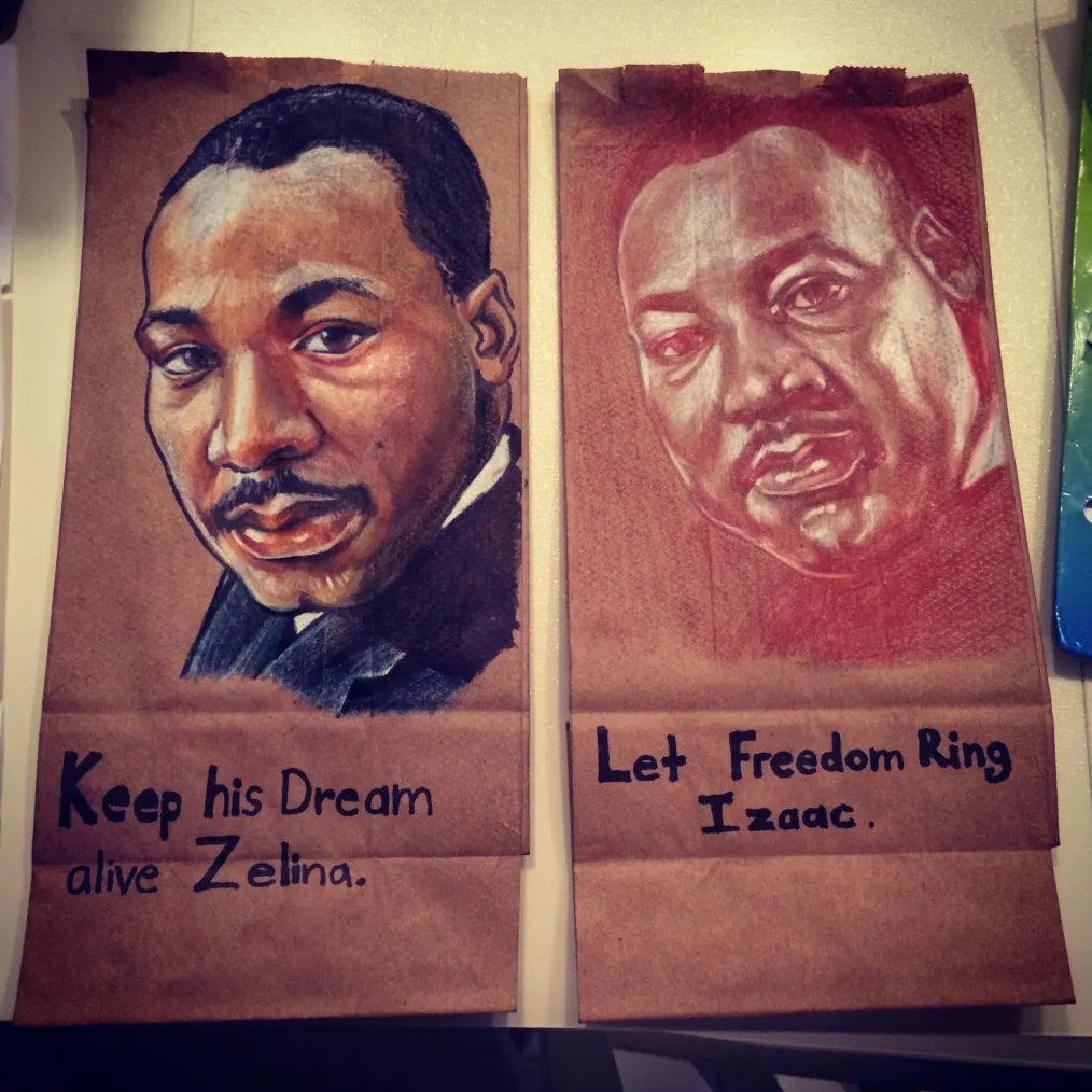 A painting on a brown paper bag of Martin Luther King, a man with a deep skin tone and short black hair with text underneath that reads "Keep His Dream Alive Zelina". Beside it is another painting on a brown paper bag of Martin Luther King with text reads "Let Freedom Ring Izaac" 