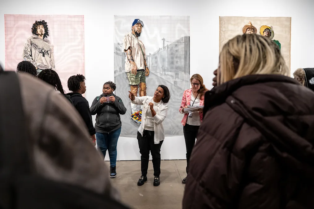 A group of young people with a range of light to dark skin tones gather around a tour guide at EXPO Chicago. 