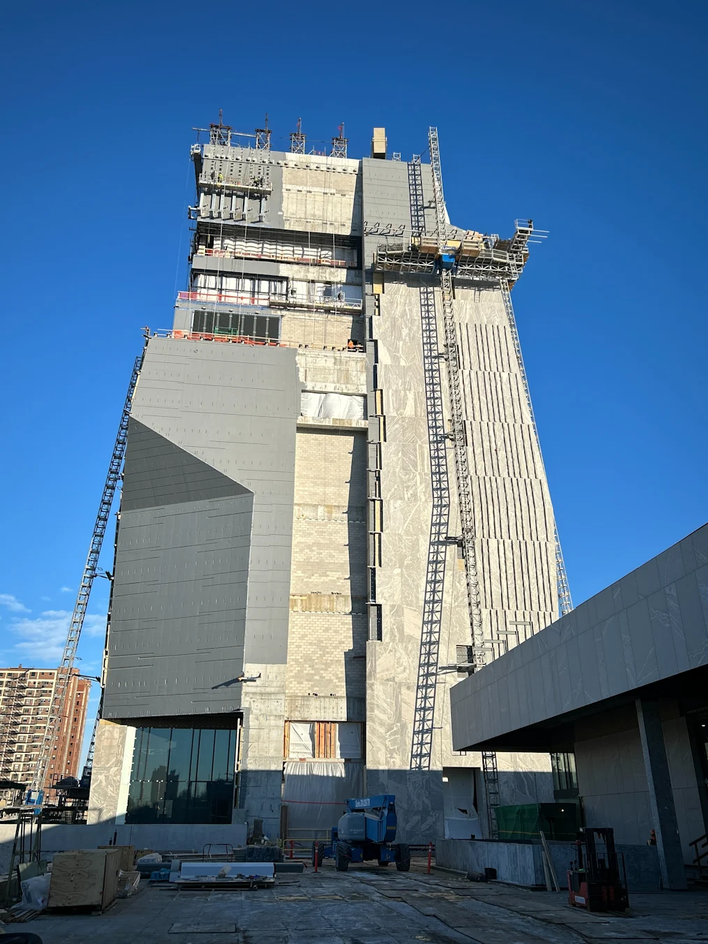 A tall, concrete and stone building under construction towers high into the sky. Scaffolding and a crane can be seen on the sides.