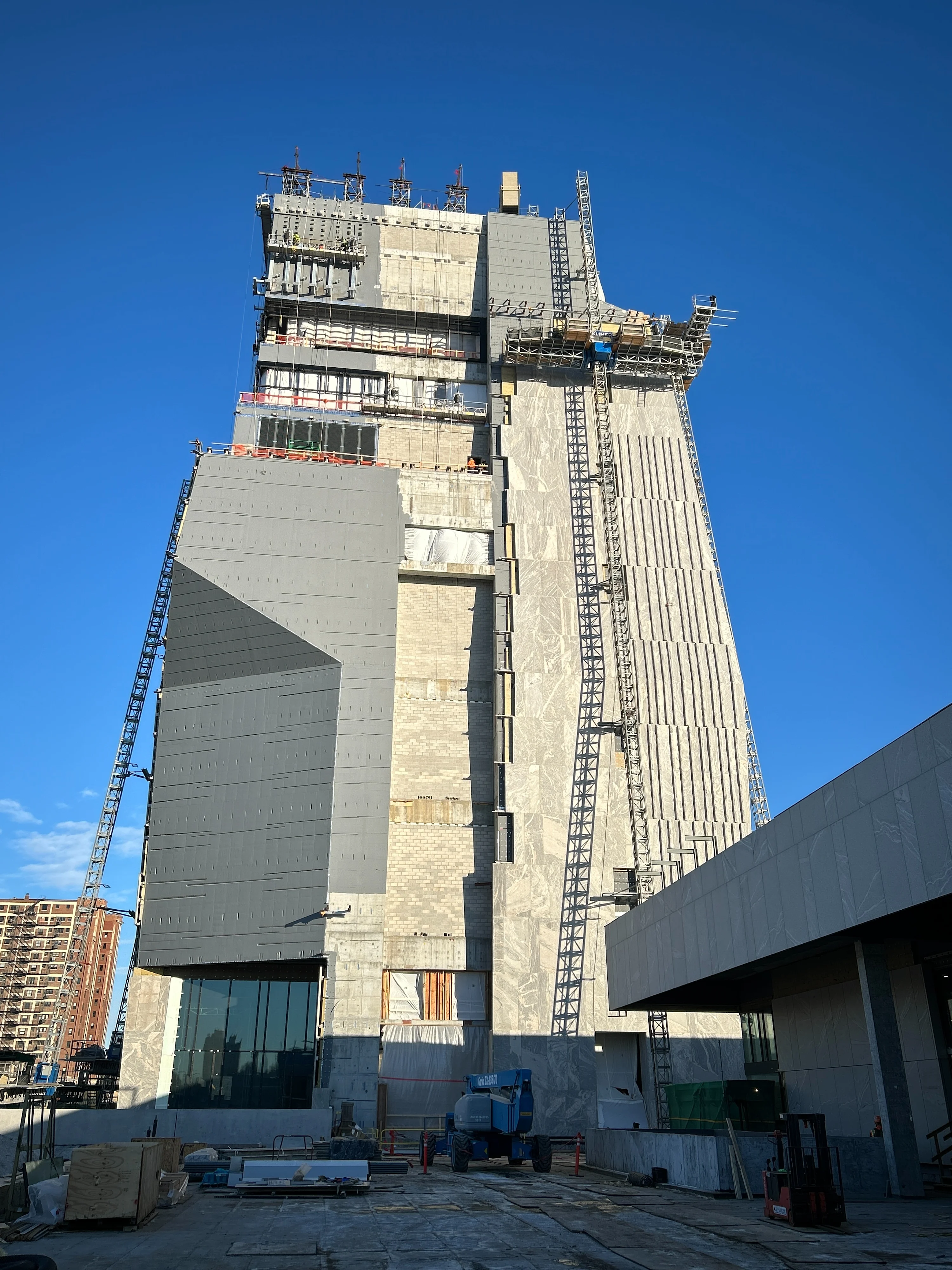 A tall, concrete and stone building under construction towers high into the sky. Scaffolding and a crane can be seen on the sides.