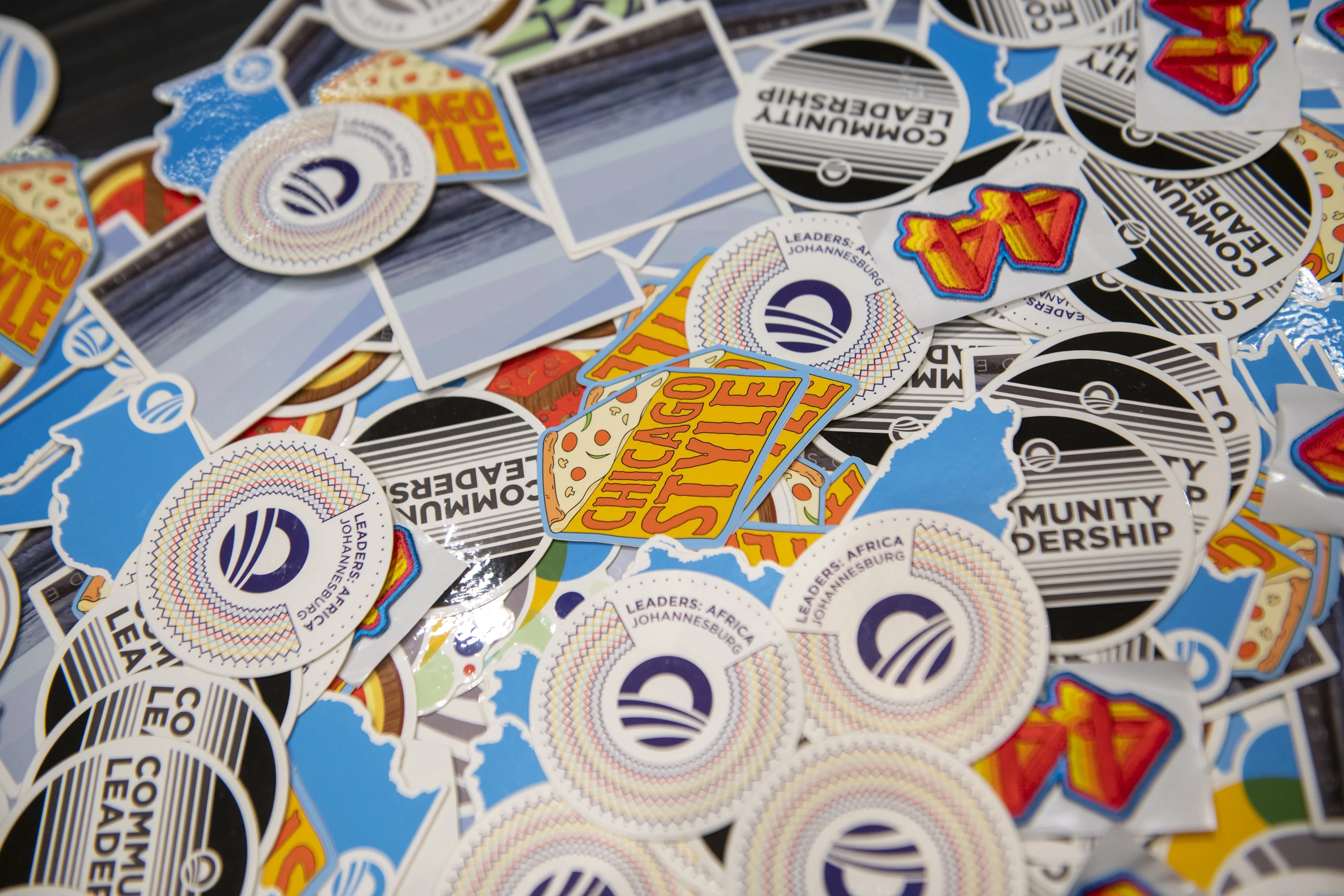 A close-up of a pile of colorful stickers. They say Community Leaders," "Chicago Style," "Leaders Africa: Johannesburg" and more.  