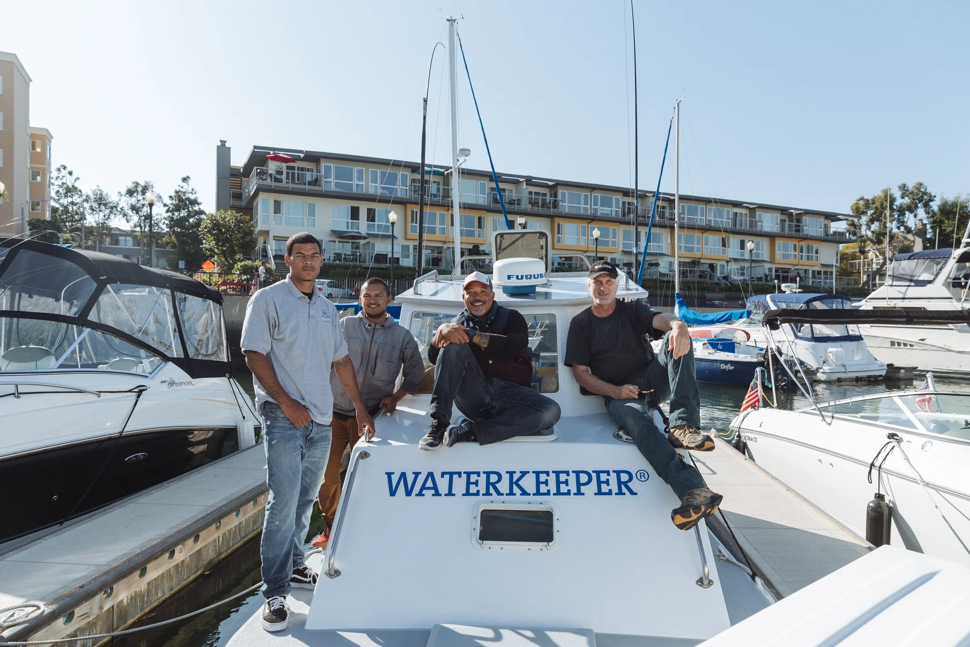 Four men of light neutral skin tone on a boat that says waterkeeper
