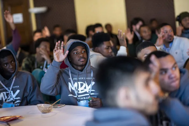 A group of young men wearing My Brothers Keeper hoodies and other appearel. Some are raising their hands.
