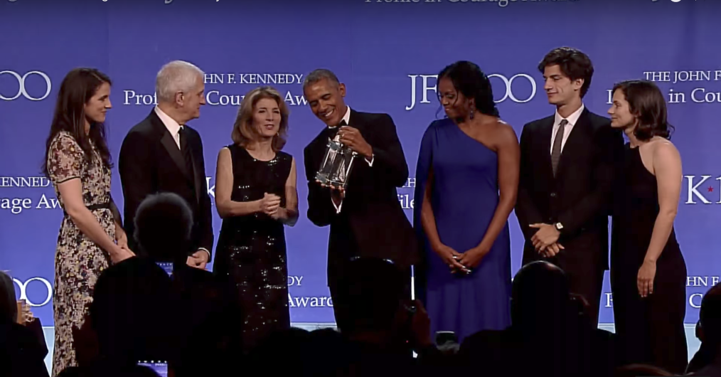 President Obama holds the John F. Kennedy Profile in Courage award. He is joined on stage by Michelle Obama and five others.