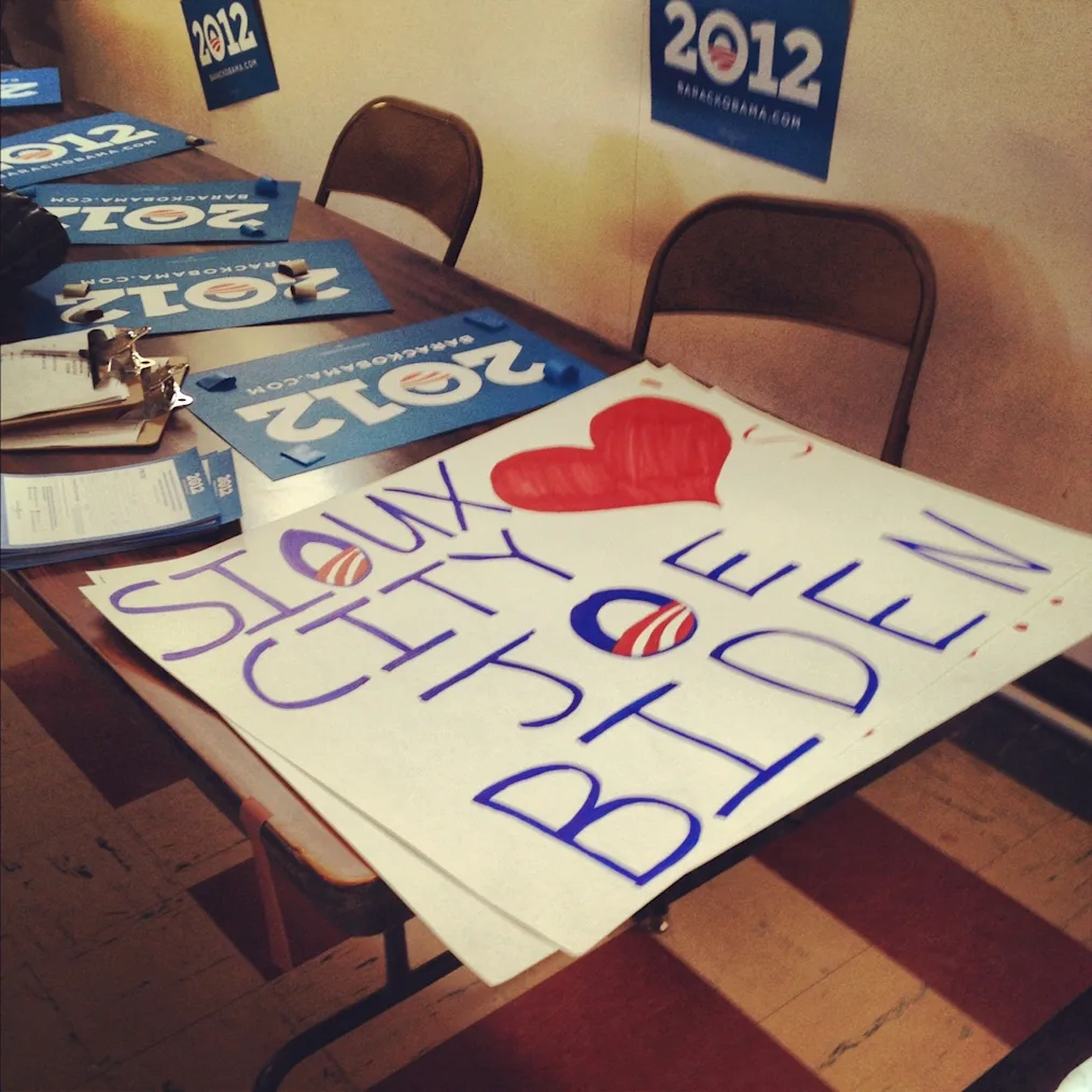 On a table, there is a display of Obama 2012 signs At the tip of the table is a sign that reads, “Sioux City loves Joe Biden.” The Obama logo is inside the Sioux and Joe. 