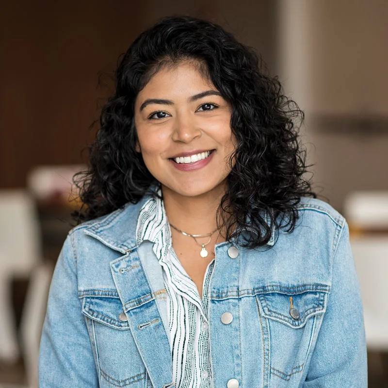 Young woman with curly hair smiles to camera.