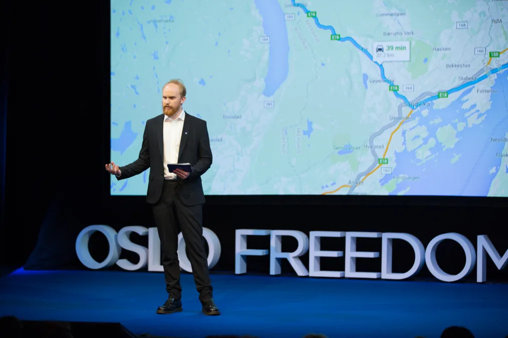 Bjørn Ihler holds a notepad as he speaks on a stage. In the background is a graphic that reads, “Oslo Freedom Forum” and a map of Norway.