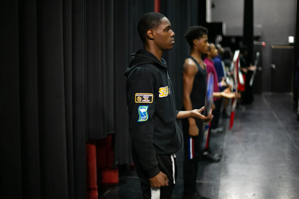 A group of young men stand in a line facing forward at their drill team practice.