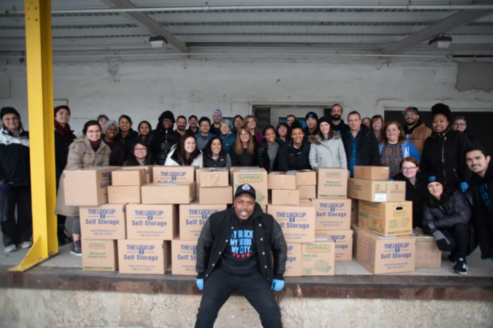 Jahmal Cole sits in front of a mountain of boxes with his volunteer staff behind them.