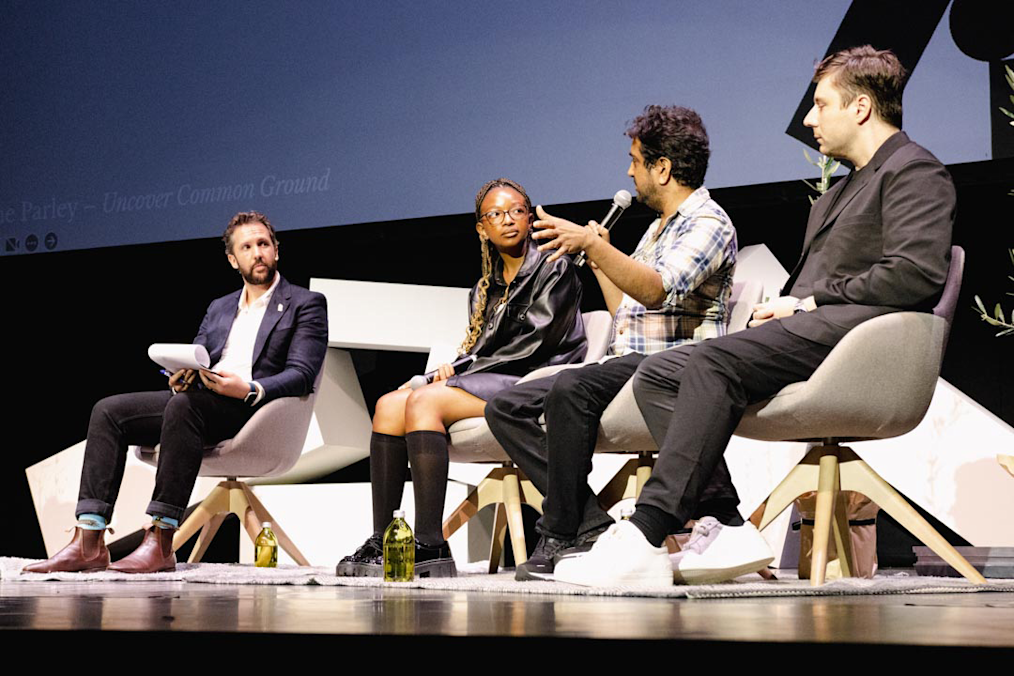 William on the left, sits on a panel with two men with light skin tones and a Black woman with a dark skin tone. They are listening to a speaker at a Parley event. 