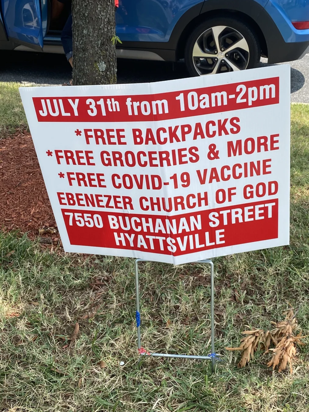 A white sign with red writing offers free backpacks, free groceries, free COVID-19 vaccines, and more.