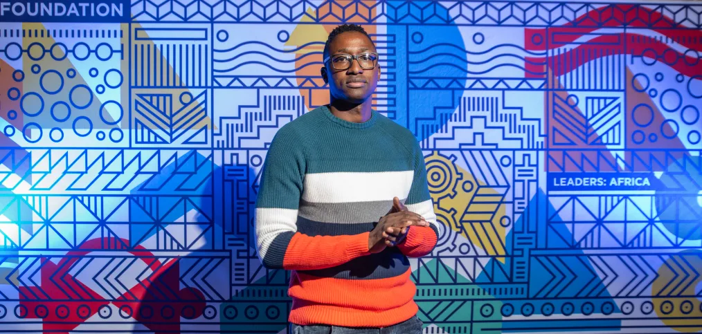 Graphic designer Osmond Tshuma poses for a photo in front of his multicolored pattern design for the Leaders: Africa program.