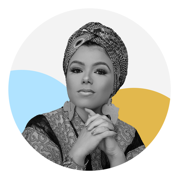 A medium skin toned woman is facing the camera with a straight expression. She is wearing a patterned headwrap, a patterned blouse and two earrings shaped like Africa. Her hands are folded in front of her. The photo is black and white and the background features two circles, one which is light blue and the other yellow.