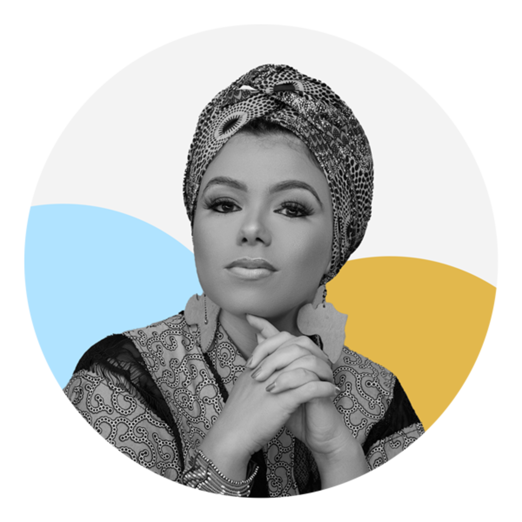A medium skin toned woman is facing the camera with a straight expression. She is wearing a patterned headwrap, a patterned blouse and two earrings shaped like Africa. Her hands are folded in front of her. The photo is black and white and the background features two circles, one which is light blue and the other yellow.