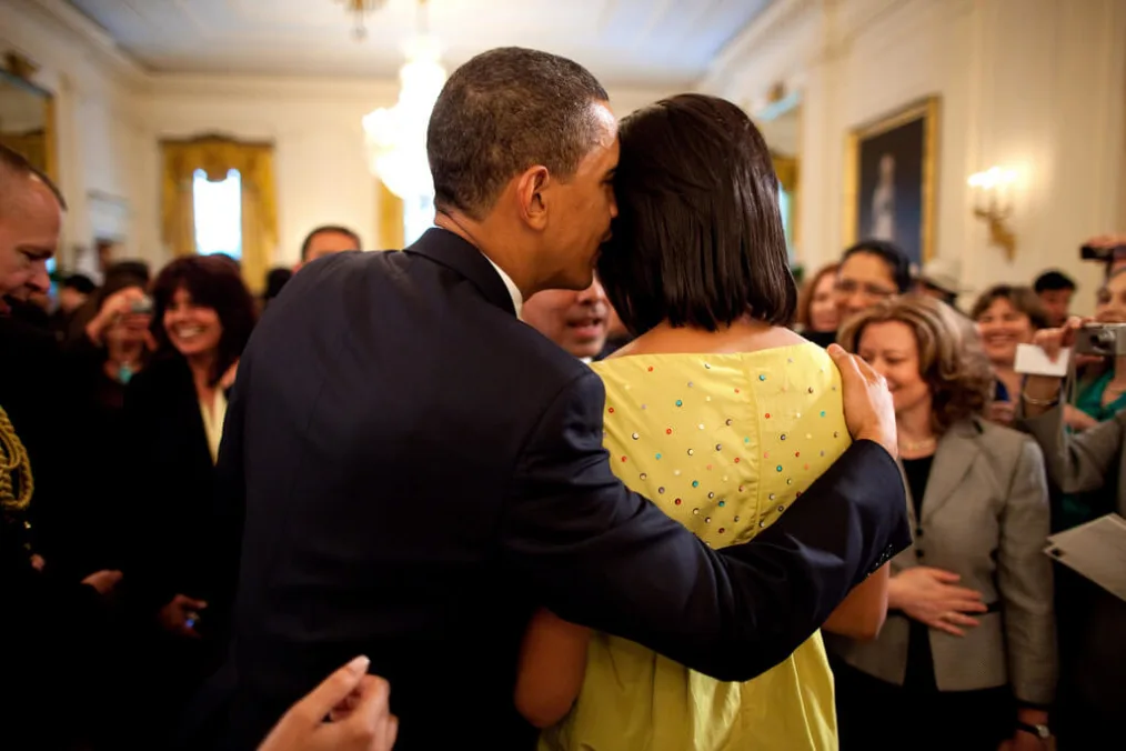 President Obama leans over to whisper in Ms.Obama´s ear in front of a crowd of people with various skin tone 