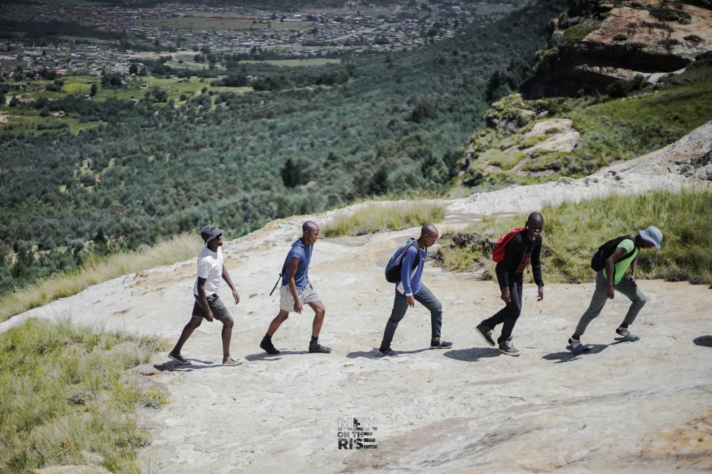 Five young men with deep skin tones hike a mountain. 