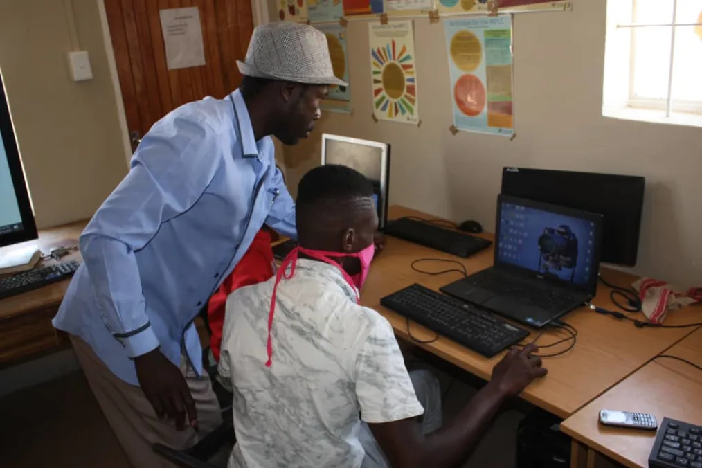 A teacher shows a young man how to use the computer