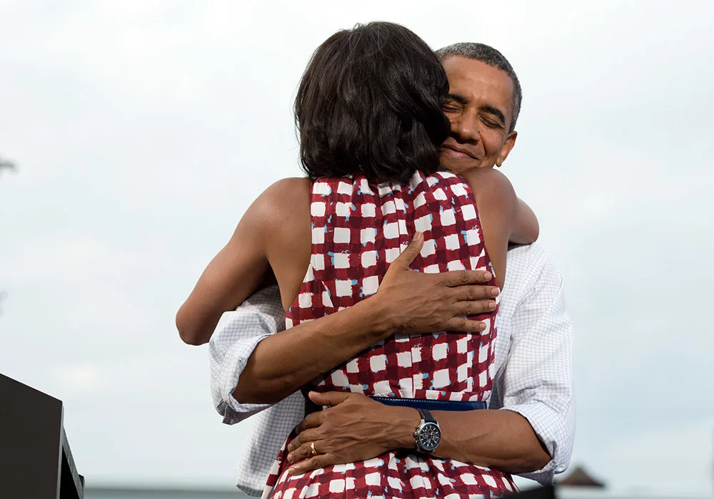 Barack Obama embracing MIchelle Obama. His eyes are closed and he has a slight smile on his face. 
