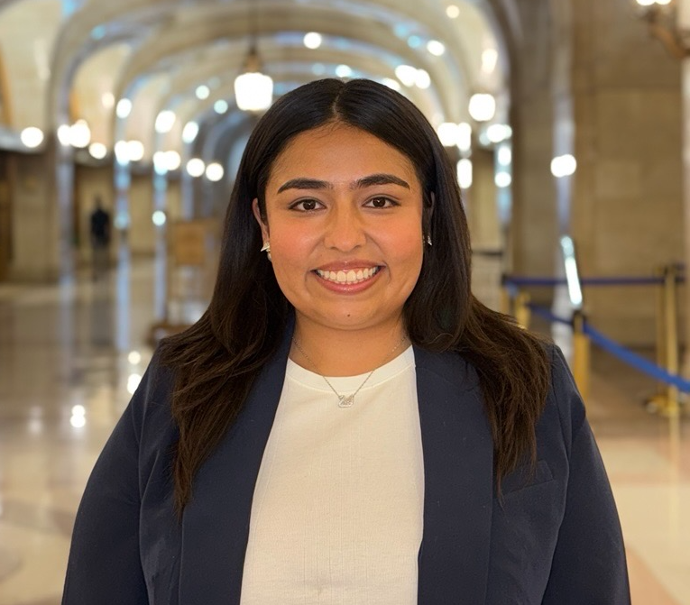 Sonia Garcia, a woman with a medium skin tone, smiles at the camera. She is wearing a navy blazer and a white top.