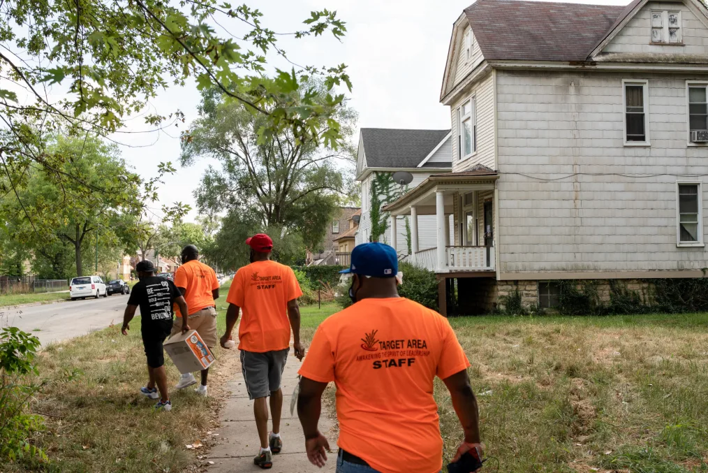 A team of outreach workers walks through a neighborhood in bright orange shirts.