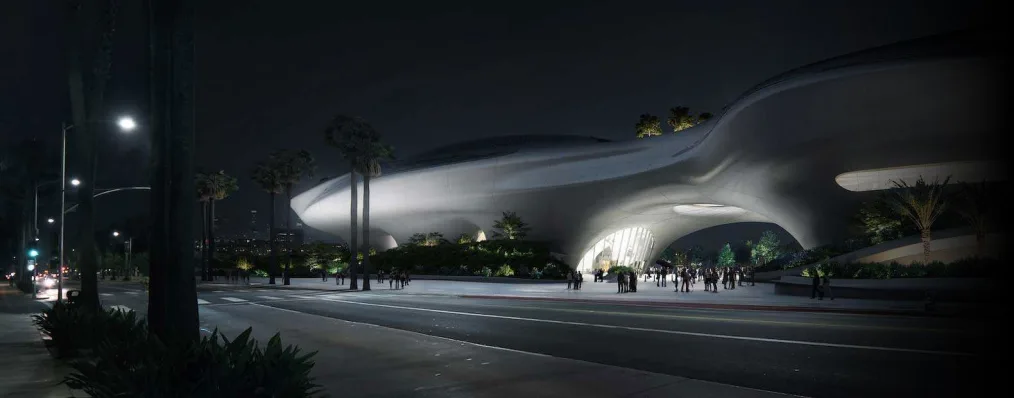 Rendering of the Lucas Museum of Narrative Art. The picture is of the museum at night. The museum is shaped like a space ship with two protruding domes. The color of the museum is white and silver. Surrounding the museum is a street and in the background of the museum is the Los Angeles, California skyline.