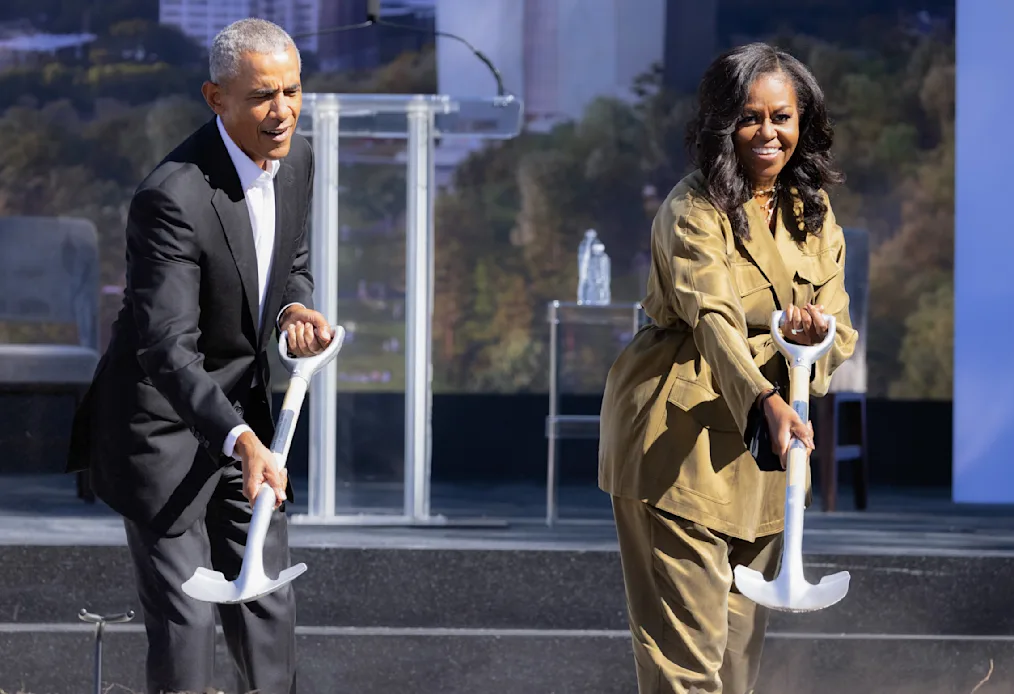 President Obama and former First Lady Michelle Obama hold shovels and smile to camera.