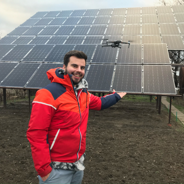 Filip Koprčina, a man with a light skin tone and dark brown hair, poses near a solar panel grid. He is smiling and wearing a red windbreaker jacket.