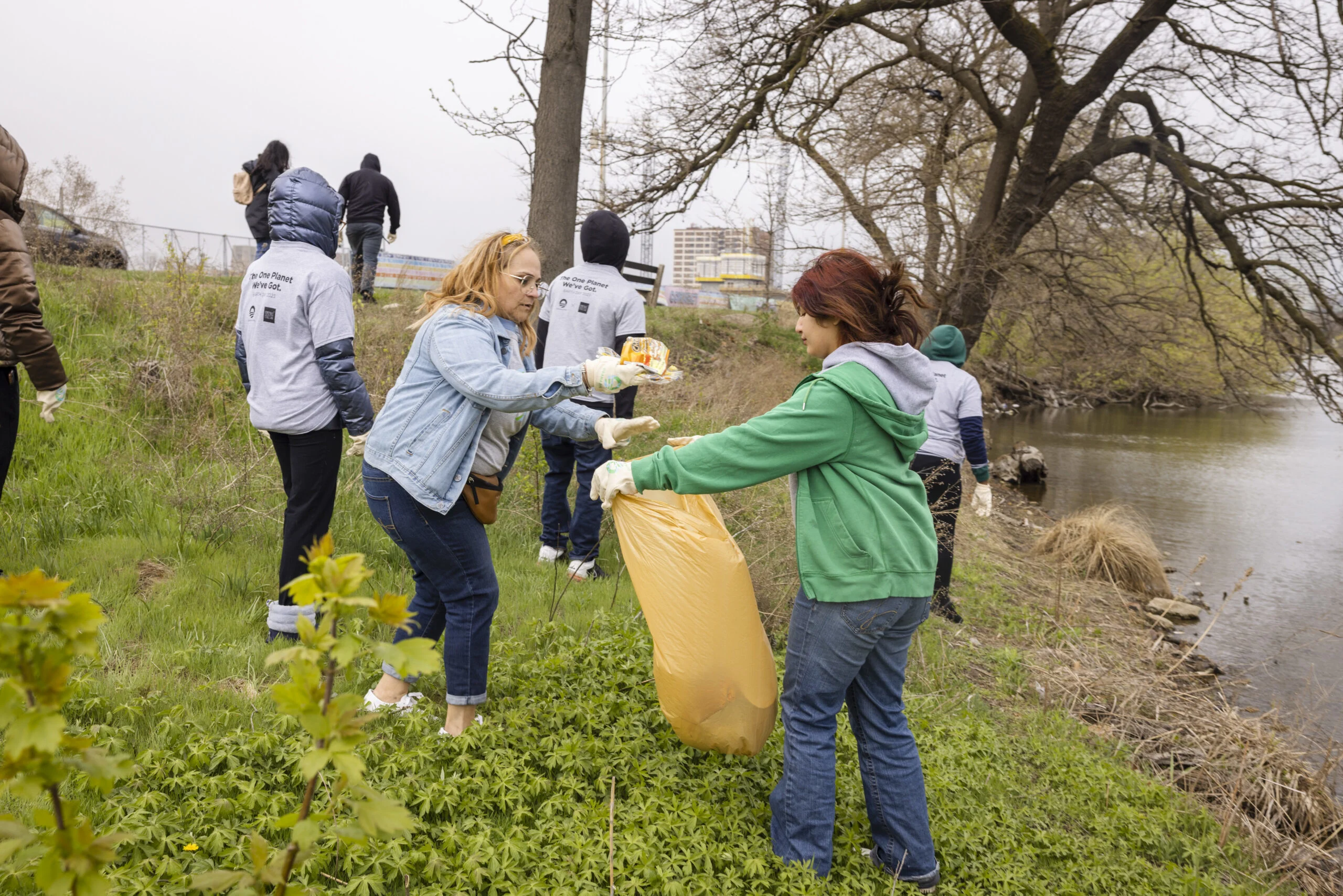 On a cloudy day, eight volunteers stand near water as they clean up trash around Jackson Park in Chicago.