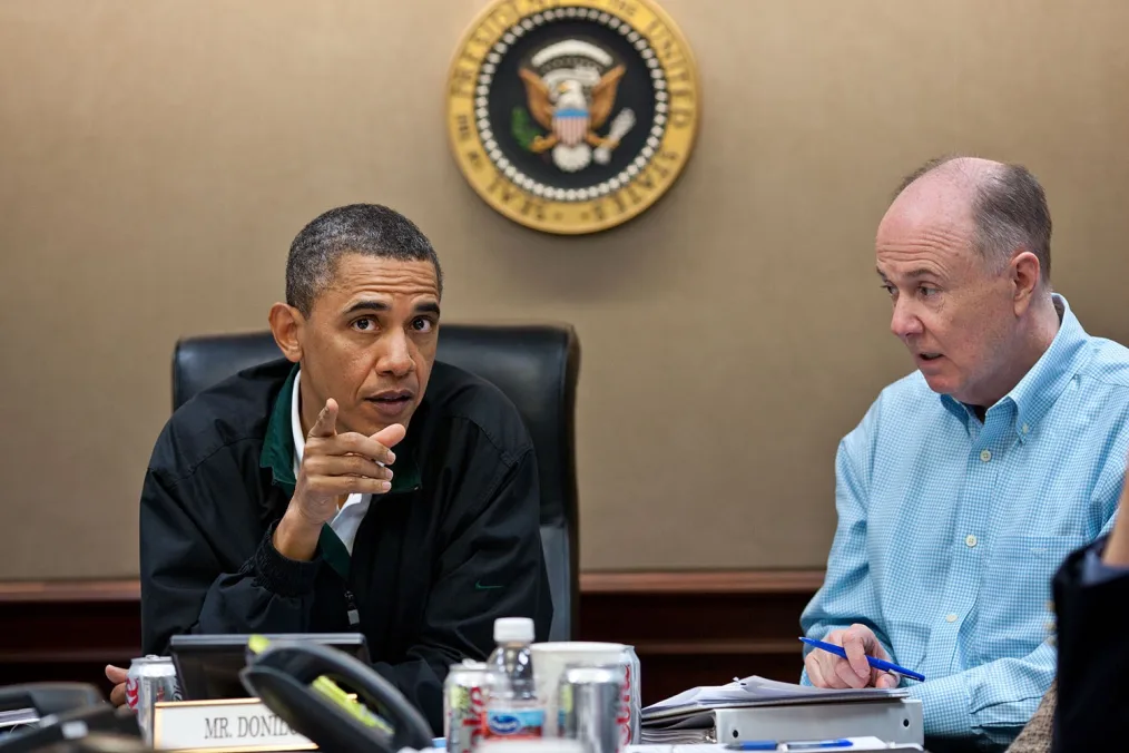 President Obama sits in the situation room, talking to a man in a blue collared shirt.