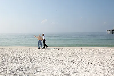 This illustration shows two men one with a medium-deep skin tone the other with a light skin tone on a beach walking together.