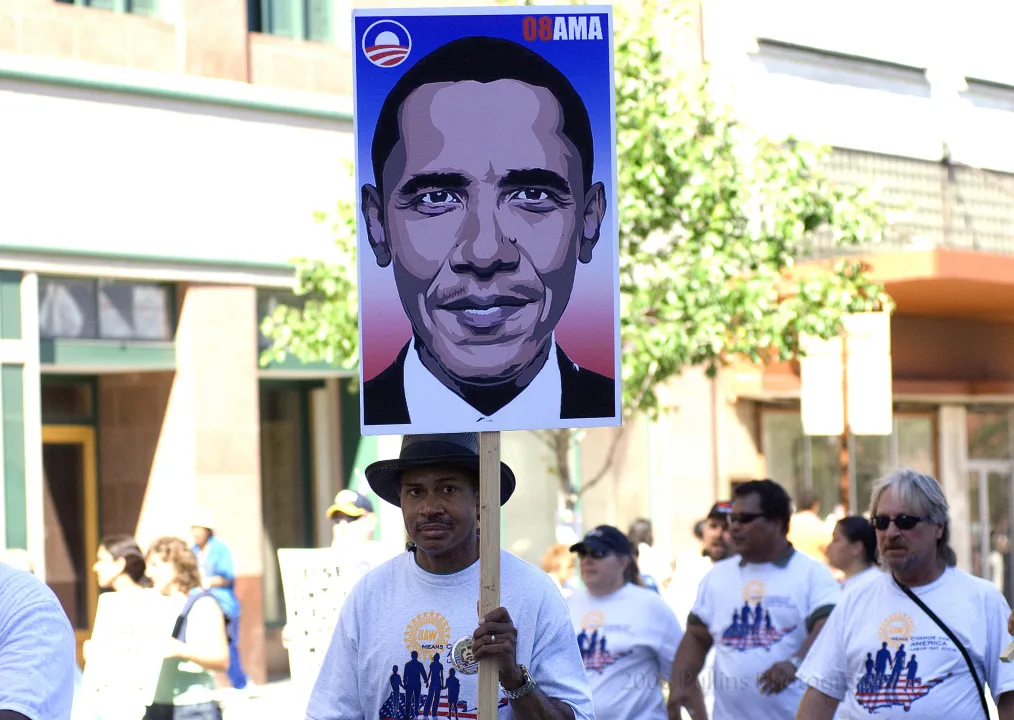 Man wearing a black hat carries a sign with a photo of then-Senator Obama in 2008.