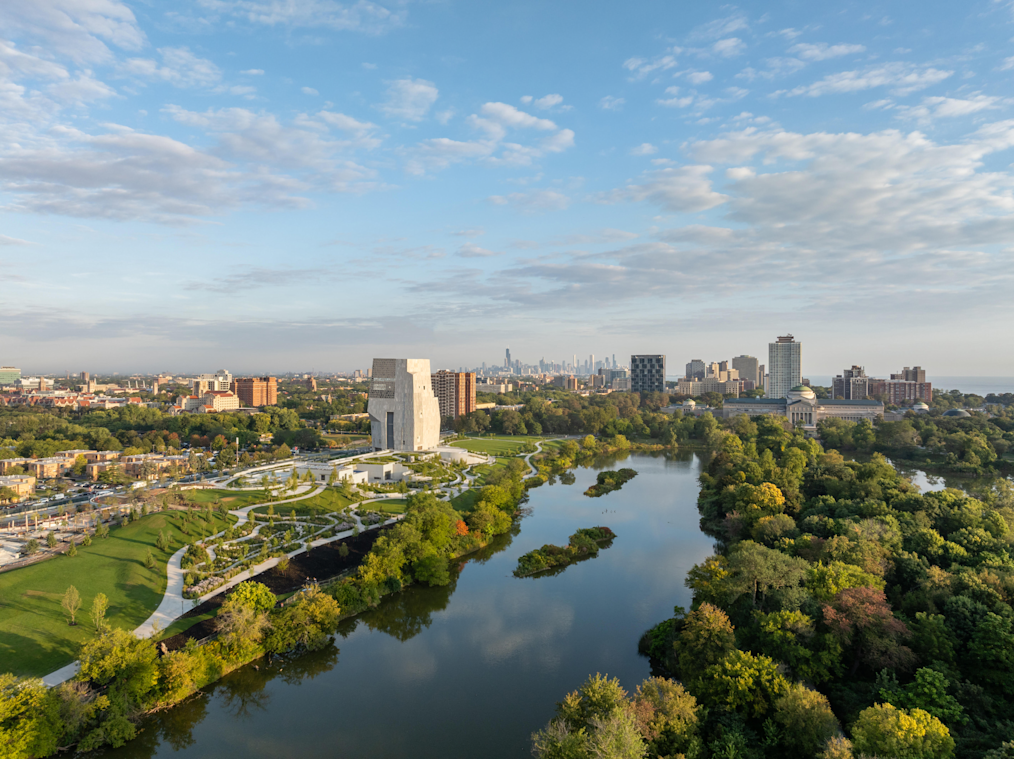 An aerial wide shot of the 19-3 acre campus at the Obama Presidential Center on a sunny and cloudy day. The picture includes an aerial view of Jackson Park and the Chicago skyline. 