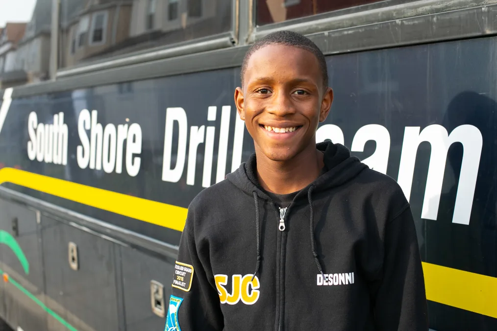 A boy smiles to camera in front of the South Shore Drill Team bus.