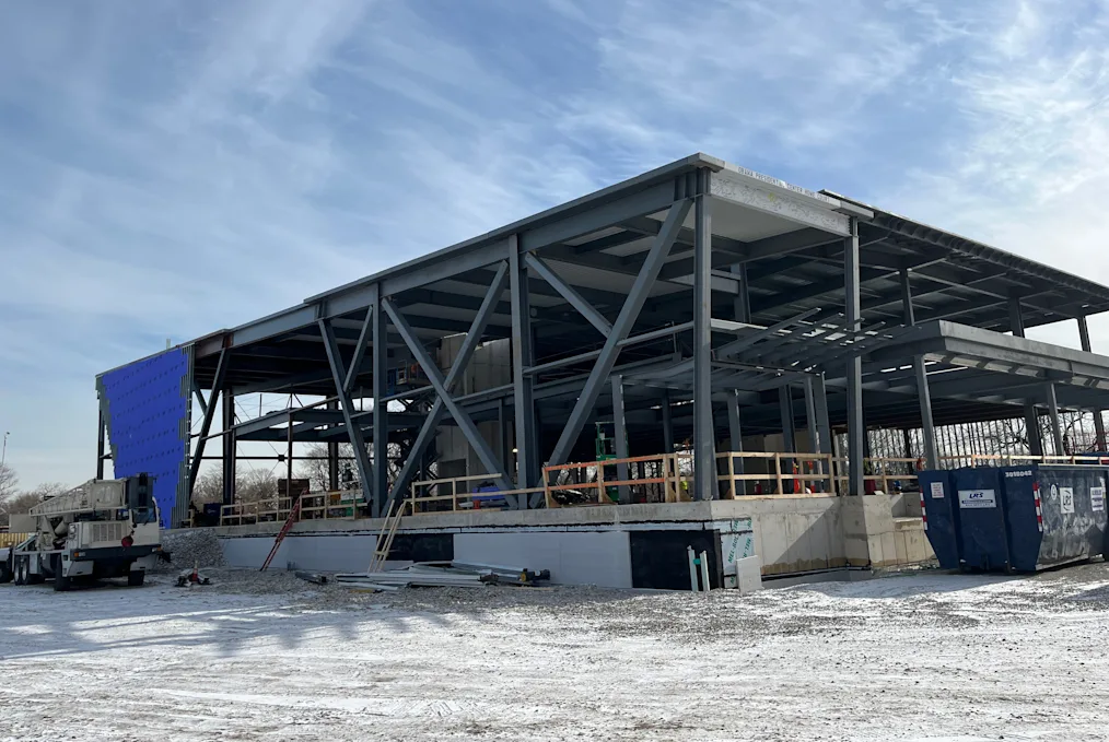 A large rectangular building under construction with steel beams and blue tarp. The walls are still open to the outside.