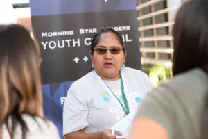 A close up of a woman with a warm light skin tone wearing a light grey shirt and black shades at a youth event 