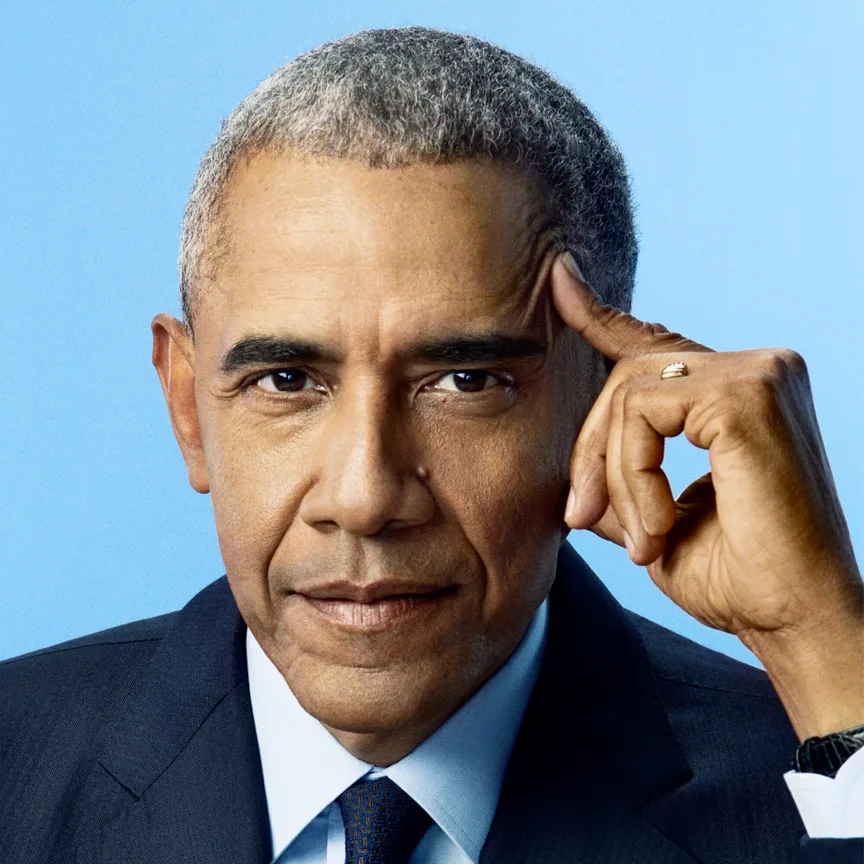 President Barack Hussein Obama is a Black man with a medium warm skin tone, and stands 6 feet 2 inches. He has a slender face, full eyebrows, and oval-shaped eyes. In this photo, he has short black and gray crew cut hair and wears a dark suit, a blue-patterned tie, and an American flag pin on his left lapel. His left hand rests on the side of his face.