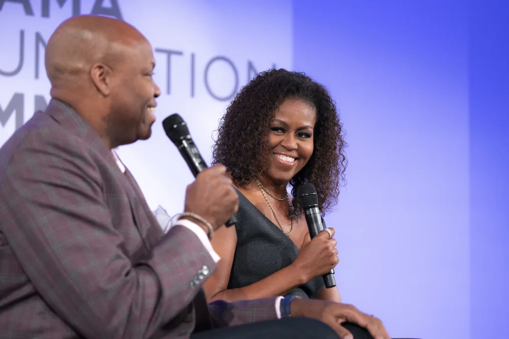 Mrs. Obama gives a knowing smile to her older brother, Craig, as he speaks into a mic.