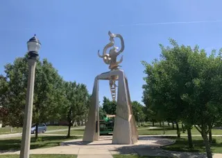 An abstract sculpture set in the middle of a park with a blazing blue sky behind it.