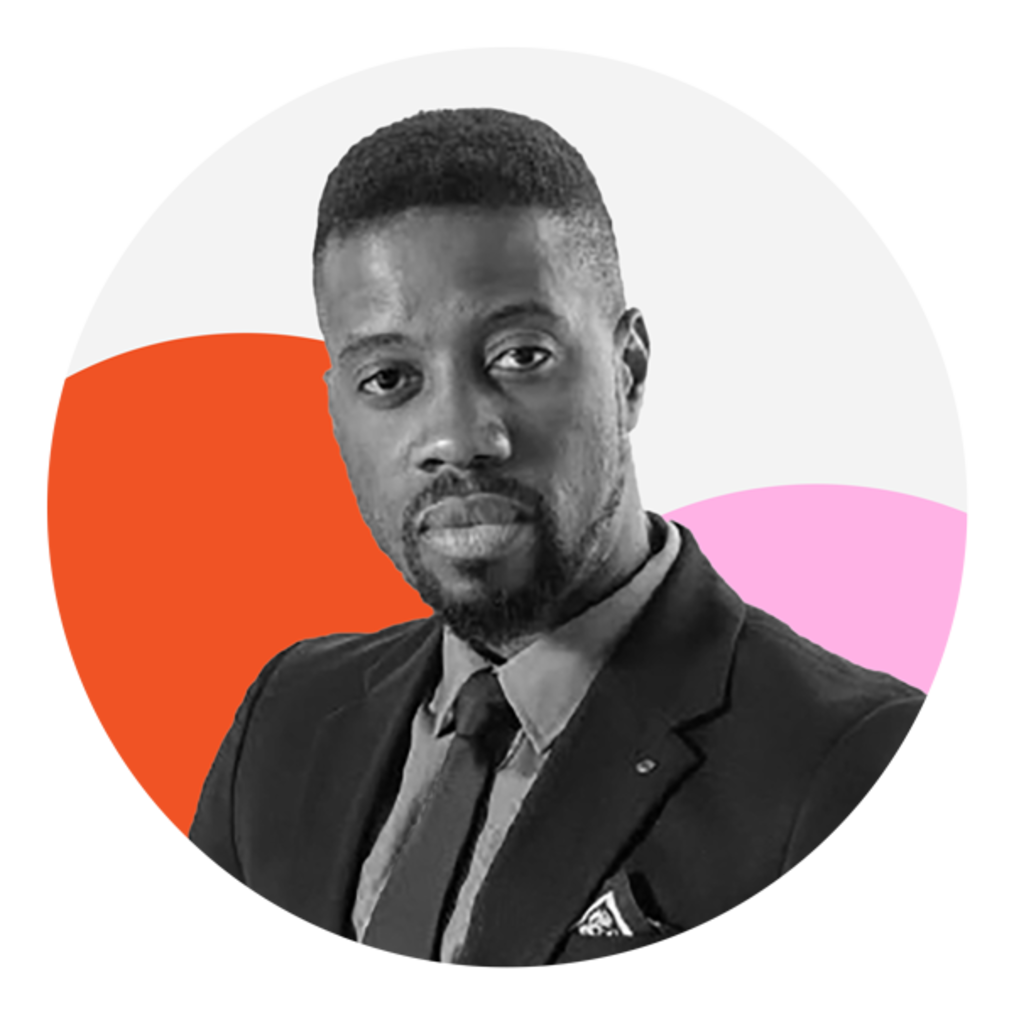A Black man with short afro hair is facing the camera with a straight expression. He is wearing a dark suit with a lighter collared shirt and a dark tie. The photo is black and white and the background features two circles, one which is orange and the other pink. 