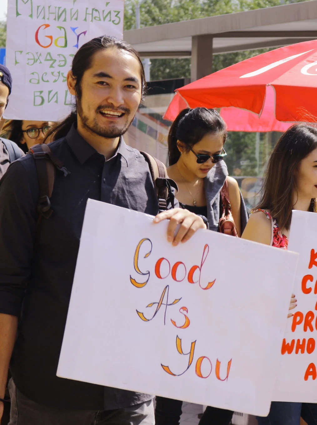 People who are holding pride signs, a man with a light golden skin tone is holding a sign that says "good as you"